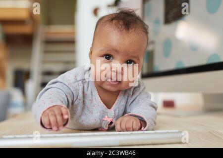 Portrait de face d'un bébé afro-américain mignon regardant l'appareil photo tout en rampant sur le bureau à domicile, espace de travail de copie Banque D'Images