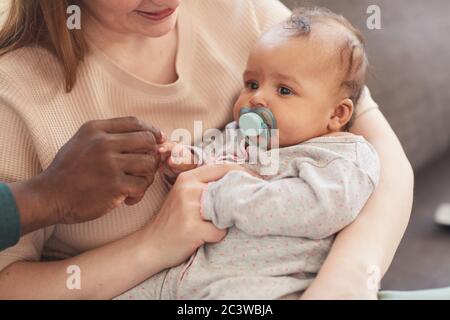 Portrait aux tons chaleureux d'une famille interraciale heureuse qui profite de son séjour à la maison, avec un père afro-américain tenant une petite main de bébé, un espace de copie Banque D'Images