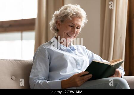 Femme mûre souriante profiter de temps libre de lecture intéressant livre Banque D'Images