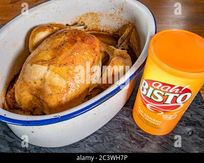 Un bac de petits morceaux de sauce au poulet Bisto à côté d'un poulet entier fraîchement cuit dans un plat à rôtir. Banque D'Images