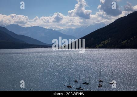Le soleil brille à la surface du lac Resia (Reschensee, Lago di Resia) avec les spectaculaires montagnes enneigées au-delà, Resia, Italie Banque D'Images