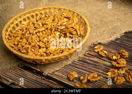 Noix pelées dans un panier en osier et noix pelées éparpillées sur une table en bois recouvertes de toile de jute à texture rugueuse. Une alimentation saine. Régime de remise en forme. Fermer Banque D'Images