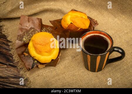 Deux petits gâteaux frais, une tasse de café et des morceaux de sucre de canne brun sur un chiffon de style maison à texture rugueuse. Gros plan Banque D'Images