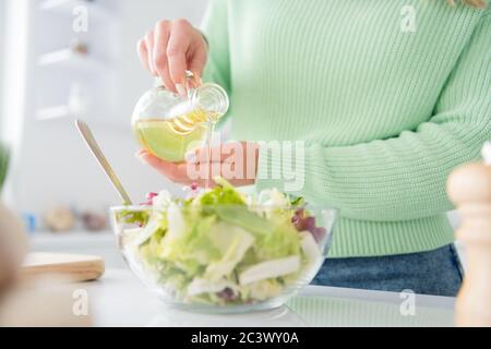 Courte vue en gros plan portrait de sa elle belle fille attrayante faire maison délicieux déjeuner atelier de passe-temps ajoutant huile légumes salade dans la lumière moderne Banque D'Images