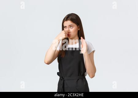 Concept des employés d'épicerie, des petites entreprises et des cafés. Mécontent et dérangé, le barista féminin se ferme le nez et grimace d'une odeur horrible Banque D'Images