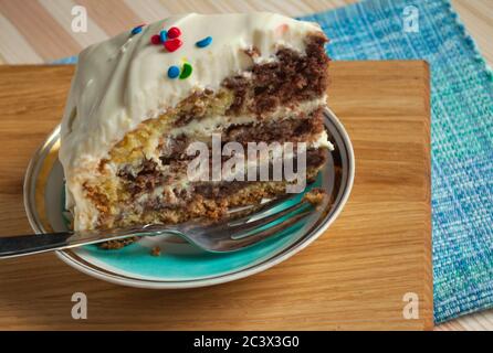 Un morceau de gâteau de chocolat avec crème sur une plaque blanche gros plan décoré avec des garnitures multicolores sur un fond en bois Banque D'Images