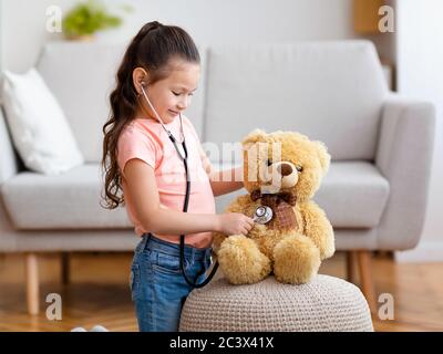 Enfant fille jouant Docteur en utilisant stéthoscope traitement de l'ours en peluche en intérieur Banque D'Images