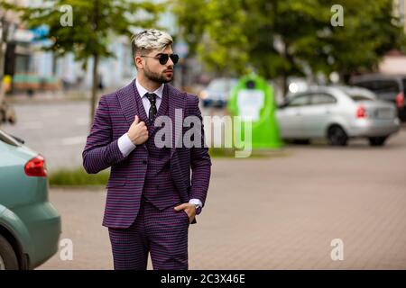 homme en lunettes et costume trois pièces violet de luxe, noeud papillon posant dans la rue Banque D'Images
