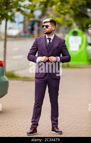 homme en lunettes et costume trois pièces violet de luxe, noeud papillon posant dans la rue Banque D'Images