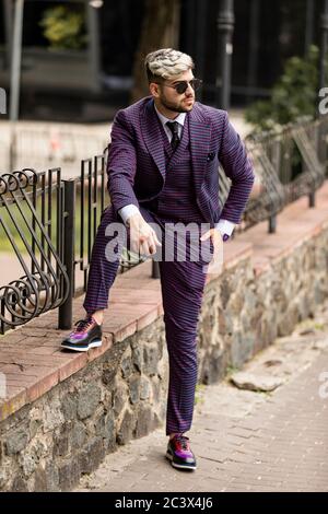 homme en lunettes et costume trois pièces violet de luxe, noeud papillon posant dans la rue Banque D'Images