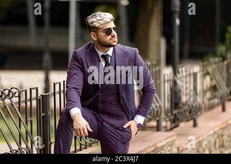 homme en lunettes et costume trois pièces violet de luxe, noeud papillon posant dans la rue Banque D'Images