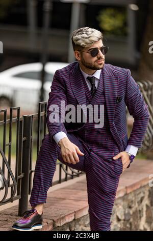 homme en lunettes et costume trois pièces violet de luxe, noeud papillon posant dans la rue Banque D'Images