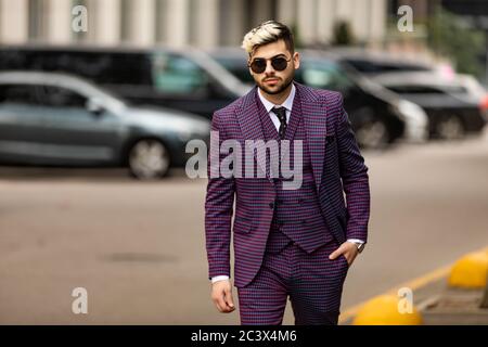 homme en lunettes et costume trois pièces violet de luxe, noeud papillon posant dans la rue Banque D'Images