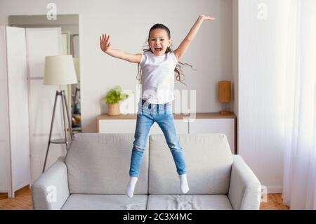 Une petite fille joyeuse qui saute sur un canapé s'amuser à la maison Banque D'Images