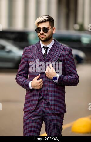 homme en lunettes et costume trois pièces violet de luxe, noeud papillon posant dans la rue Banque D'Images
