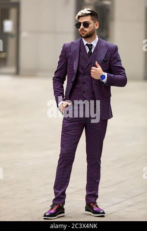 homme en lunettes et costume trois pièces violet de luxe, noeud papillon posant dans la rue Banque D'Images