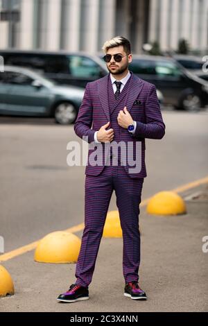 homme en lunettes et costume trois pièces violet de luxe, noeud papillon posant dans la rue Banque D'Images