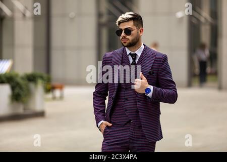 homme en lunettes et costume trois pièces violet de luxe, noeud papillon posant dans la rue Banque D'Images