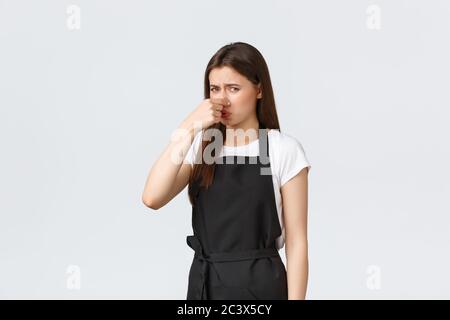 Concept des employés d'épicerie, des petites entreprises et des cafés. Mécontent et dérangé, le barista féminin se ferme le nez et grimace d'une odeur horrible Banque D'Images