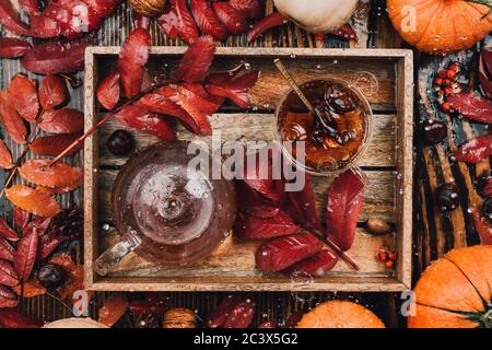 La vie d'automne encore avec tasse de thé en verre et bouilloire dans plateau en bois avec feuilles rouges, citrouilles et cendres et gouttes de pluie tombant Banque D'Images