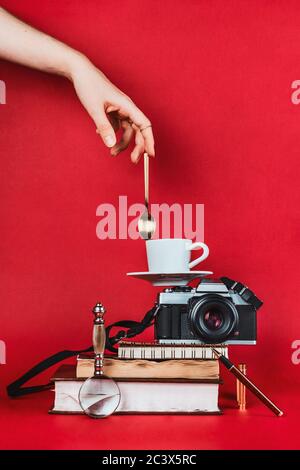 Équilibre entre la composition de la vie de la femme et des livres, appareil photo vintage, tasse de café et cuillère à la main de la femme sur fond rouge Banque D'Images