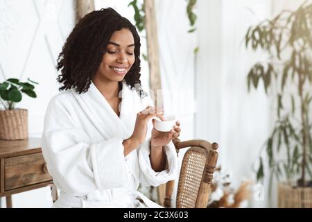 Soins de la peau. Belle fille noire après avoir fait la douche appliquer de la crème hydratante sur le visage Banque D'Images