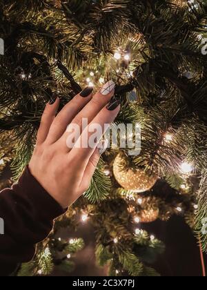 Main de femme avec une belle manucure noire et blanche touchant l'arbre de Noël avec anticipation de la fête du nouvel an. Ambiance festive. Fermer la vue Banque D'Images