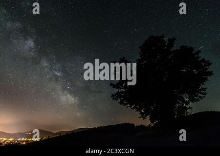 Ciel étoilé avec la galaxie de la voie lactée en été avec un arbre en face d'une ville illuminée, l'Allemagne Banque D'Images