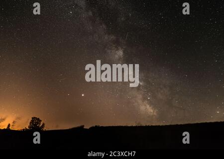 Ciel étoilé avec la galaxie de la voie lactée en été avec un arbre en face d'une ville illuminée, l'Allemagne Banque D'Images