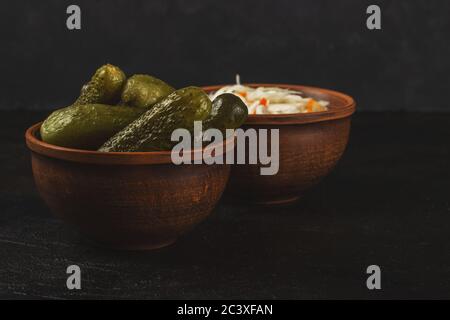 Cornichons et choucroute dans un bol en argile sur fond de béton foncé Banque D'Images