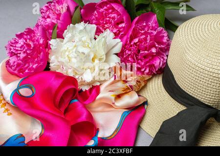 Mélanger le bouquet de pivoines, le chapeau de paille pour femme et le foulard en soie sur fond lilas. Gros plan. Banque D'Images