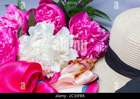 Gros plan sur un bouquet de pivoines, chapeau de paille pour femme et foulard en soie sur fond lilas. Idée de mode Banque D'Images