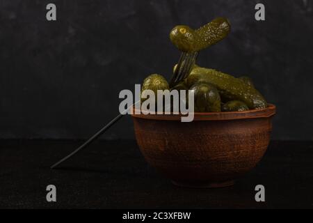 Cornichons et choucroute dans un bol en argile sur fond de béton foncé Banque D'Images