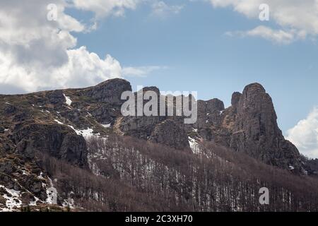 Colonnes de montagne impressionnantes, pointues, rocailleuses, arbres sans feuilles, reste de la neige sur le sol et ciel bleu avec des nuages blancs Banque D'Images