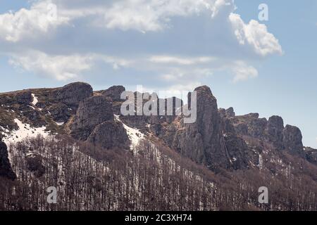 Colonnes de montagne impressionnantes, pointues, rocailleuses, arbres sans feuilles, reste de la neige sur le sol et ciel bleu avec des nuages blancs Banque D'Images