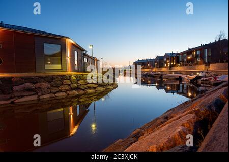 Un canal paisible avec de petits bateaux amarrés au milieu de la zone résidentielle. Photographié au coucher du soleil avec des reflets des maisons sur l'eau. Banque D'Images