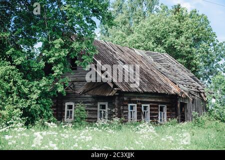 Ancienne maison rustique en bois abandonnée, en chute libre, parmi les arbres, un jour d'été et de l'herbe autour Banque D'Images