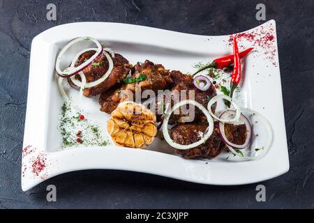 Morceaux de béliers grillés déposés sur une plaque blanche. Avec oignons, piments et ail Banque D'Images