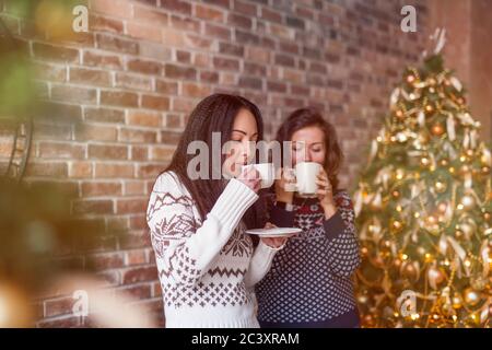 Deux amis buvant du café dans un loft avec un arbre de Noël décoré Banque D'Images