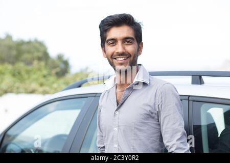Happy man smiling standing pilote par son nouveau sport voiture bleue stationnement extérieur isolé arrière-plan. Beau jeune homme heureux de son nouveau véhicule. Banque D'Images