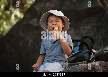En mangeant des collations saines, un jeune garçon prend un morceau d'une pomme tout en se reposant pendant une randonnée. Banque D'Images