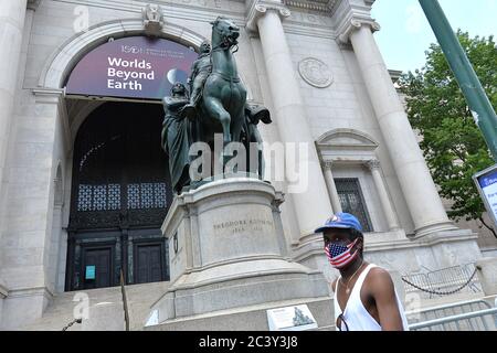 Un homme portant un masque à thème drapeau américain, à l'époque de COVID-19, passe devant la statue équestre Theodore Roosevelt, Qui se trouve à l'entrée principale du Musée américain d'histoire naturelle de Central Park West, est sur le point d'être retiré parce qu'il est offensant pour les Noirs et les Indiens d'Amérique, New York, NY, 22 juin 2020. Le retrait de la statue du 26e président américain sur un cheval, représenté par un homme amérindien d'un côté et un homme africain de l'autre, a été approuvé par le maire de New York Bill de Blasio après que le Musée ait demandé qu'il soit retiré. (Anthony Behar/ Banque D'Images