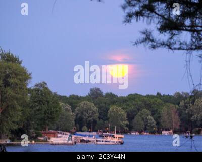 Lune qui s'élève à travers les nuages roses au-dessus d'un lac Banque D'Images