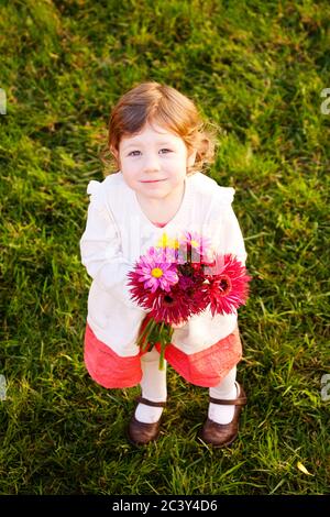 Une adorable petite fille tient un bouquet de fleurs Gerbera Daisy tout en se tenant sur l'herbe verte. Banque D'Images