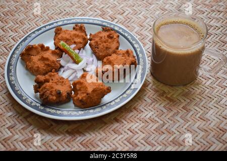 Vue latérale sur Dal vada, Masala vada, chana vada servi avec des oignons coupés et des chilins verts et thé sur le tapis de service. En-cas de cuisine indienne frite, lentilles Banque D'Images