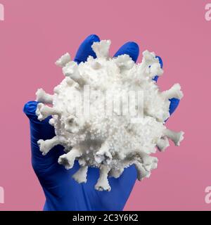 Main dans un gant en latex bleu tenant le modèle du coronavirus Banque D'Images