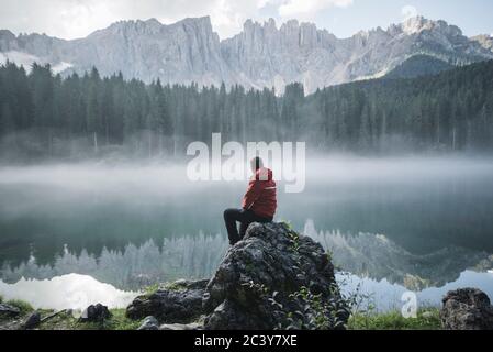 Suisse, jeune homme assis à Lago di Carezza dans les Alpes Dolomites à l'aube Banque D'Images