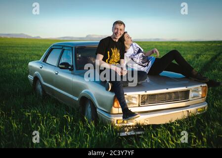 Ukraine, Crimée, couple assis sur une vieille voiture dans un paysage rural Banque D'Images