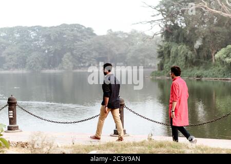 Deux jeunes marchent dans le parc en arrière-à-dos en soirée d'été. Rabindra Sarobar (Dhakuria Lake), Kolkata du Sud, État indien du Bengale occidental, Calc Banque D'Images