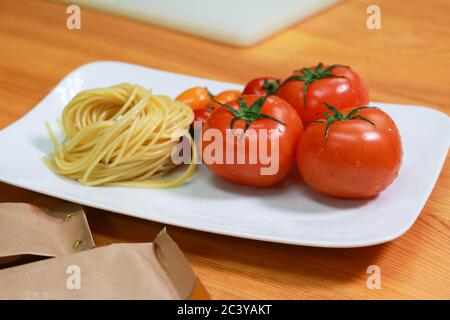 Pâtes crues aux tomates fraîches sur une assiette blanche. Des ingrédients frais de spaghetti sur la table en bois. Banque D'Images